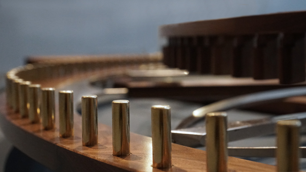 Large wooden wall sculpture made from walnut, brass and gold leaf, featuring three slow-rotating circular wheels set within a geometric framework. Handcrafted with fine cabinetmaking techniques, the piece is motorized for silent, continuous movement.