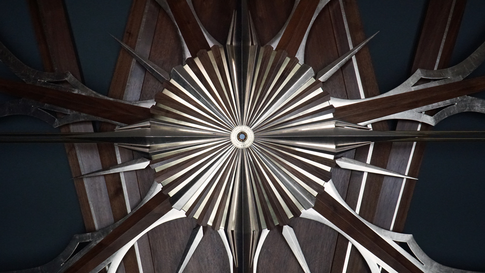Large wooden wall sculpture made from walnut, brass and gold leaf, featuring three slow-rotating circular wheels set within a geometric framework. Handcrafted with fine cabinetmaking techniques, the piece is motorized for silent, continuous movement.